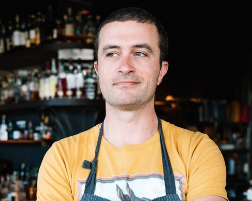  A man wearing a kitchen apron stands in a restaurant. 