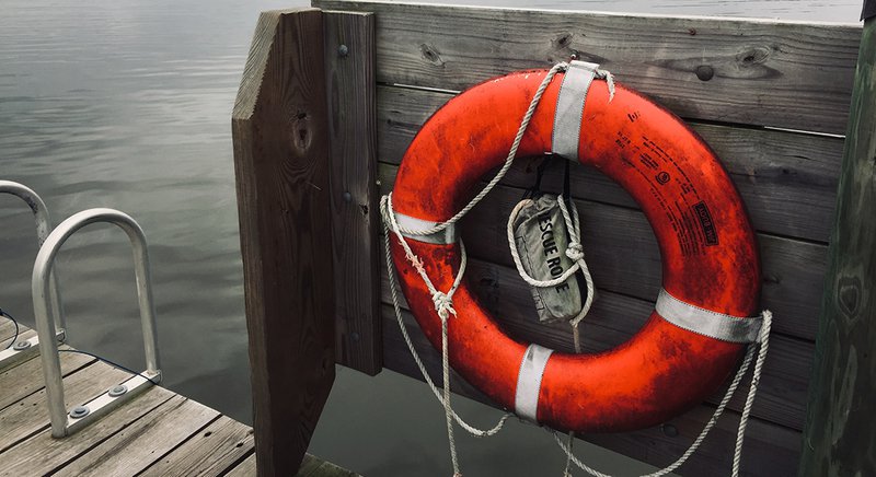  An orange life-preserver ring hangs on a wooden post near a large body of water. 