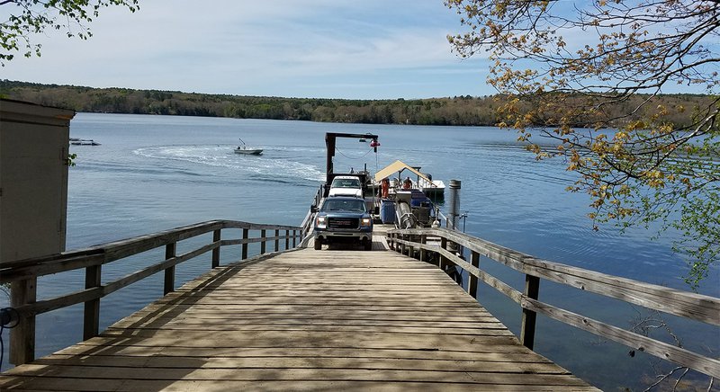  A truck backs down a long dock to the edge of a body of water. 